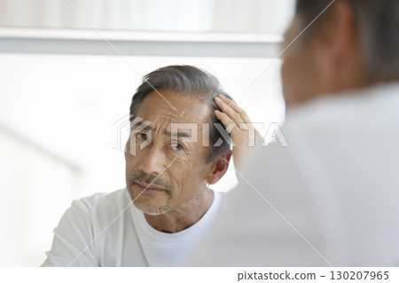 一位 60 多歲的男子照鏡子，擔心自己的髮際線 130207965