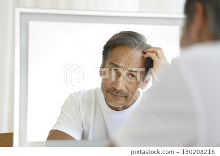 A man in his 60s looking in the mirror and worrying about his hairline A man in his 60s looking in the mirror and worrying about his hairline 130208218