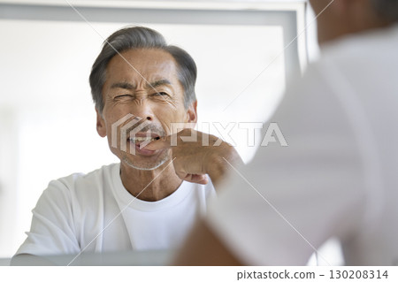 Senior man looking in the mirror and worrying about his gums 130208314