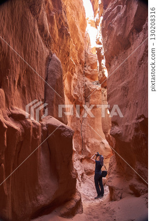 Tourist explores the Narrow Slot Canyon with its vibrant red rock formations 130208316