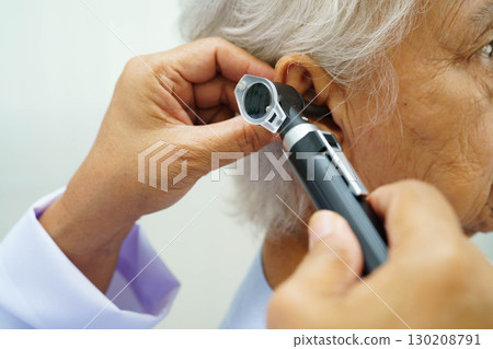 Otolaryngologist or ENT physician doctor examining senior patient ear with otoscope, hearing loss problem. 130208791