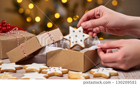 Christmas star-shaped cookies with icing packed in a gift box, held by hands against a festive bokeh background 130209581