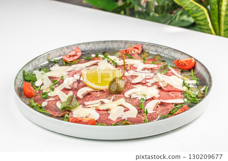 Beef carpaccio with parmesan, arugula, mushrooms, and lemon served on a round plate 130209677