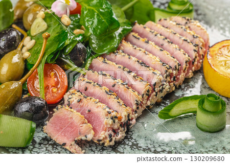 Seared tuna with sesame seeds, fresh salad, olives, and lemon on a ceramic plate 130209680