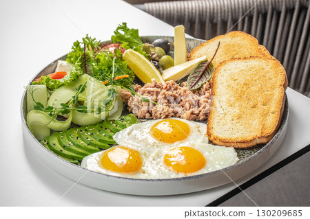 Breakfast plate with fried eggs, tuna, avocado, toast, cheese, and fresh vegetables 130209685