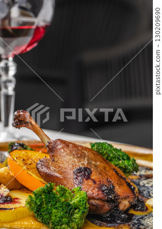 Baked duck leg with broccoli and orange slices served with sauce and wine 130209690