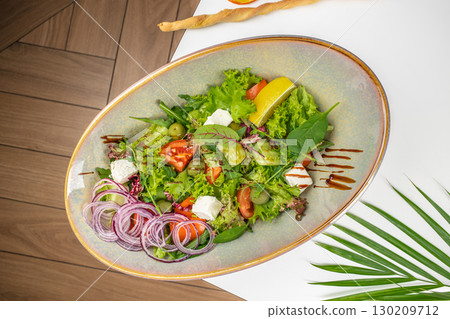 Fresh vegetable salad with feta cheese, red onion, olives, and lemon served on a ceramic plate Fresh vegetable salad with feta cheese, red onion, olives, and lemon served on a ceramic plate 130209712