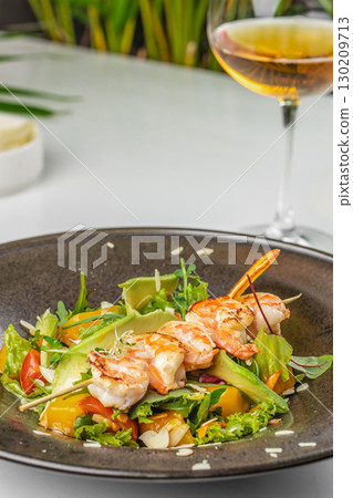 Grilled shrimp skewers with fresh vegetable salad and avocado served on a dark plate 130209713