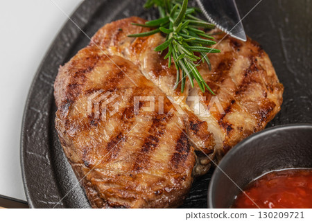 Close up of grilled beef steak with rosemary and sauce on a black plate 130209721