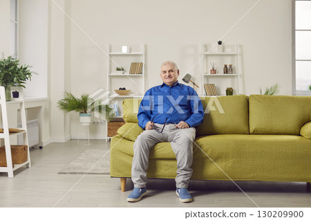 Optimistic elderly man sitting on sofa at home 130209900