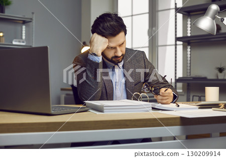 Male auditor or accountant gets tired while working with documents in the office Male auditor or accountant gets tired while working with documents in the office 130209914