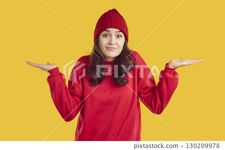 Clueless woman in red sweatshirt and hat shrugs shoulders isolated on yellow background Clueless woman in red sweatshirt and hat shrugs shoulders isolated on yellow background 130209978