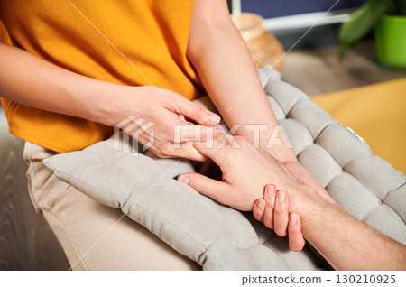 Masseuse making thai yoga massage. Woman therapist doing traditional massage treatment, stretching male patient's body. Client enjoying hand massage in calm atmosphere. Cropped view. 130210925