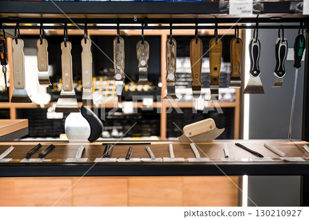 Wooden and plastic handled spatula tools hanging on display in a hardware store, used for stretch ceiling installation and PVC film fitting. 130210927