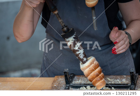Prague,Czech Republic,August 6,2023.A stall prepares and sells the typical national dessert,chimney cake, or trdlo in the local language. Female hands remove the finished products from the baking tray 130211295