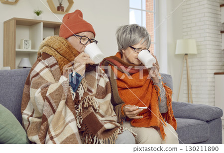 Sick senior couple covered in blankets sitting on sofa at home with seasonal flu or cold. Sick senior couple covered in blankets sitting on sofa at home with seasonal flu or cold. 130211890