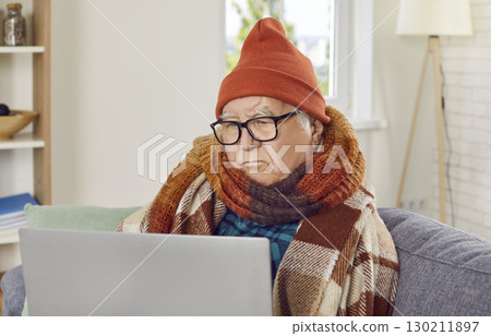 Senior frozen man using laptop while sitting on couch in the living room at home. Senior frozen man using laptop while sitting on couch in the living room at home. 130211897