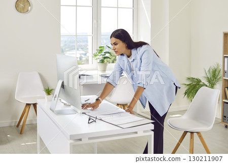 Young business woman accountant working on pc computer with tables at office. Young business woman accountant working on pc computer with tables at office. 130211907