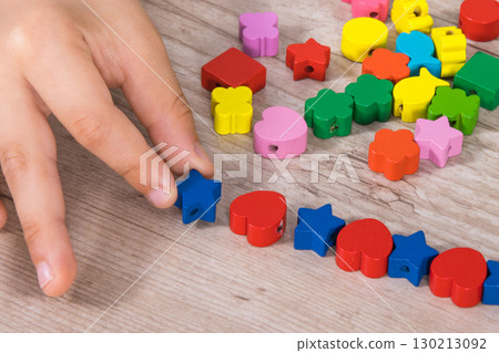 Hands of kid making bracelet from thread and colored beads 130213092