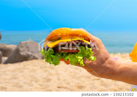 Man holding burger in a hand against beach background 130215102