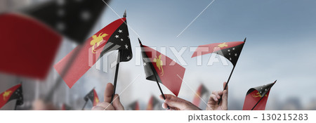 Papua New Guinea flags in their hands on a blurred urban background Papua New Guinea flags in their hands on a blurred urban background 130215283