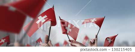 Switzerland flags in their hands on a blurred urban background Switzerland flags in their hands on a blurred urban background 130215405