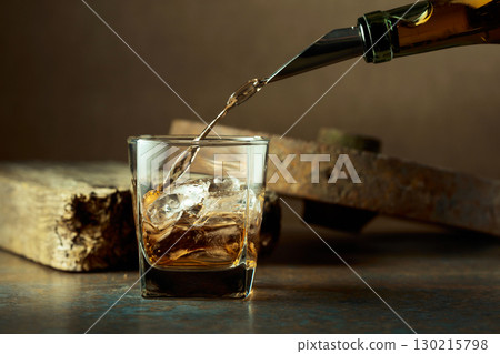 Whiskey is poured from a bottle into a frozen glass with natural ice. Whiskey is poured from a bottle into a frozen glass with natural ice. 130215798
