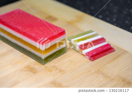 Colorful striped layered jelly candy, a traditional sweet Indonesian Kue Lapis dessert, neatly cut on a wooden board, ready for a festive celebration Colorful striped layered jelly candy, a traditional sweet Indonesian Kue Lapis dessert, neatly cut on a wooden board, ready for a festive celebration 130216117