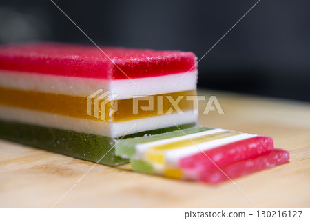 Vibrant layered jelly candy block with cut slices, showcasing red, white, yellow, and green colors, representing delicious confectionery treat or festive snack 130216127
