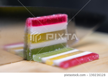 Vibrantly layered jelly candy, like pate de fruit, sliced on a wooden board, showcasing its unique texture and sparkling sugar coating, a sweet confectionery treat Vibrantly layered jelly candy, like pate de fruit, sliced on a wooden board, showcasing its unique texture and sparkling sugar coating, a sweet confectionery treat 130216128