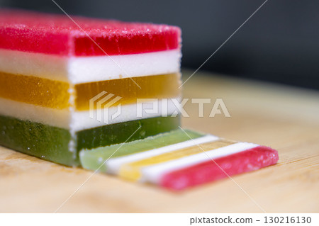 Delicious vibrant layered jelly dessert features a freshly cut slice displaying its colorful red, white, yellow, and green layers, ideal for sweet indulgence 130216130