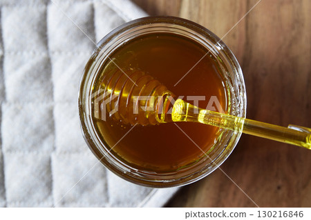 Honey big glass jar with honeycomb and yellow spoon stay on the wood table with rustic napkin. 130216846