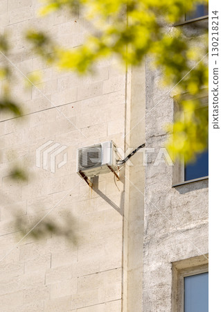 air conditioner on wall of an apartment building with view of green trees.  130218214