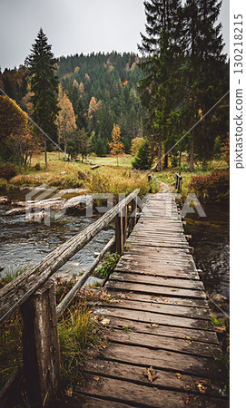 Old wooden bridge over river, surrounded by autumn forest  130218215