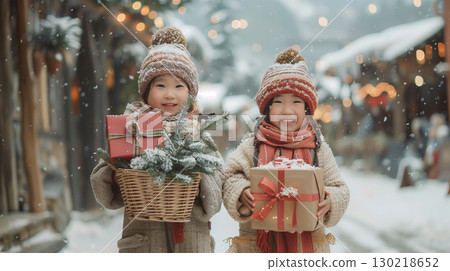 Two little asian girls in winter clothes holding Christmas gifts on snowy street 130218652