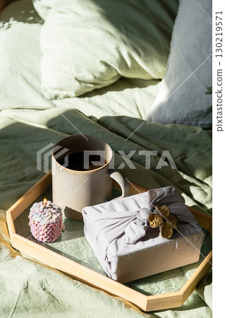 Breakfast tray with coffee mug, lit candle and furoshiki gift on bed. Breakfast tray with coffee mug, lit candle and furoshiki gift on bed. 130219571