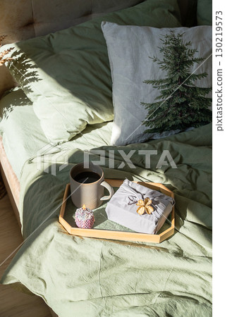 Wooden tray with coffee, candle and gift present on bed duvet. Wooden tray with coffee, candle and gift present on bed duvet. 130219573