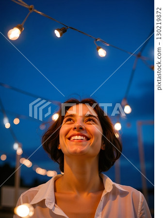 Person in a white shirt stands under glowing string lights at dusk - ai generated 130219872