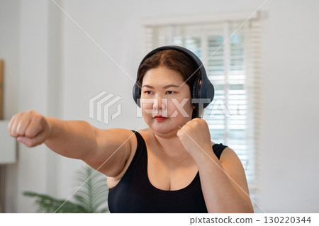 Determined plus-size woman practicing fitness boxing at home, embracing wellness and healthy lifestyle Determined plus-size woman practicing fitness boxing at home, embracing wellness and healthy lifestyle 130220344