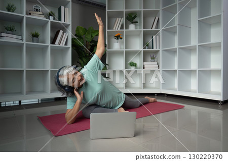 Senior woman engaging in yoga with headphones and laptop in a modern wellness space Senior woman engaging in yoga with headphones and laptop in a modern wellness space 130220370