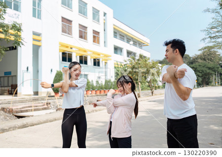 Family demonstrating warm-up exercises outdoors, daughter playfully following her parents' lead Family demonstrating warm-up exercises outdoors, daughter playfully following her parents' lead 130220390