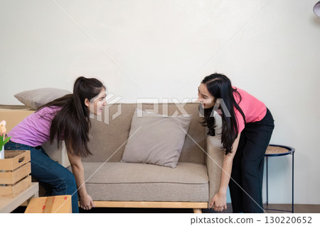 LGBT couple joyfully moving a couch together into their new home, teamwork on display 130220652