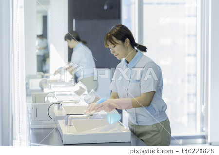 一名年輕的女清潔工正在擦拭辦公大樓浴室的水槽。照片提供：東京電子專門學校、電波學園 130220828