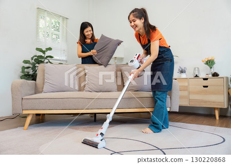 Housekeeping service with two women vacuuming and arranging pillows. 130220868