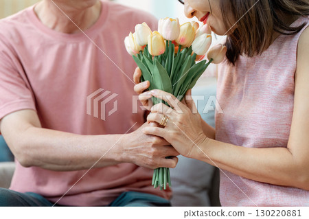 Senior couple sharing a tender moment with a bouquet of tulips on Valentine's Day in their cozy living room Senior couple sharing a tender moment with a bouquet of tulips on Valentine's Day in their cozy living room 130220881