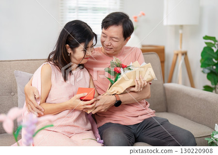 Senior couple celebrating Valentine's Day with a gift and flowers in a cozy living room 130220908