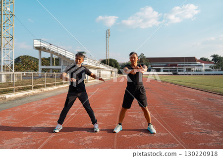 Two senior men performing wellness exercises and stretching at the athletic track 130220918
