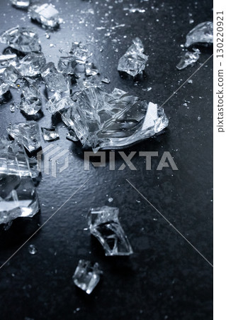 Shattered glass fragments on dark surface reflecting light 130220921
