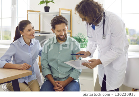 Friendly gynecologist advises couple on pregnancy and shows them clipboard with test results. 130220933