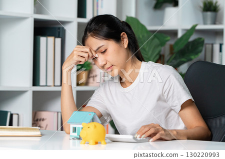 Stressed homebuyer analyzing finances and savings with calculator and piggy bank at desk Stressed homebuyer analyzing finances and savings with calculator and piggy bank at desk 130220993